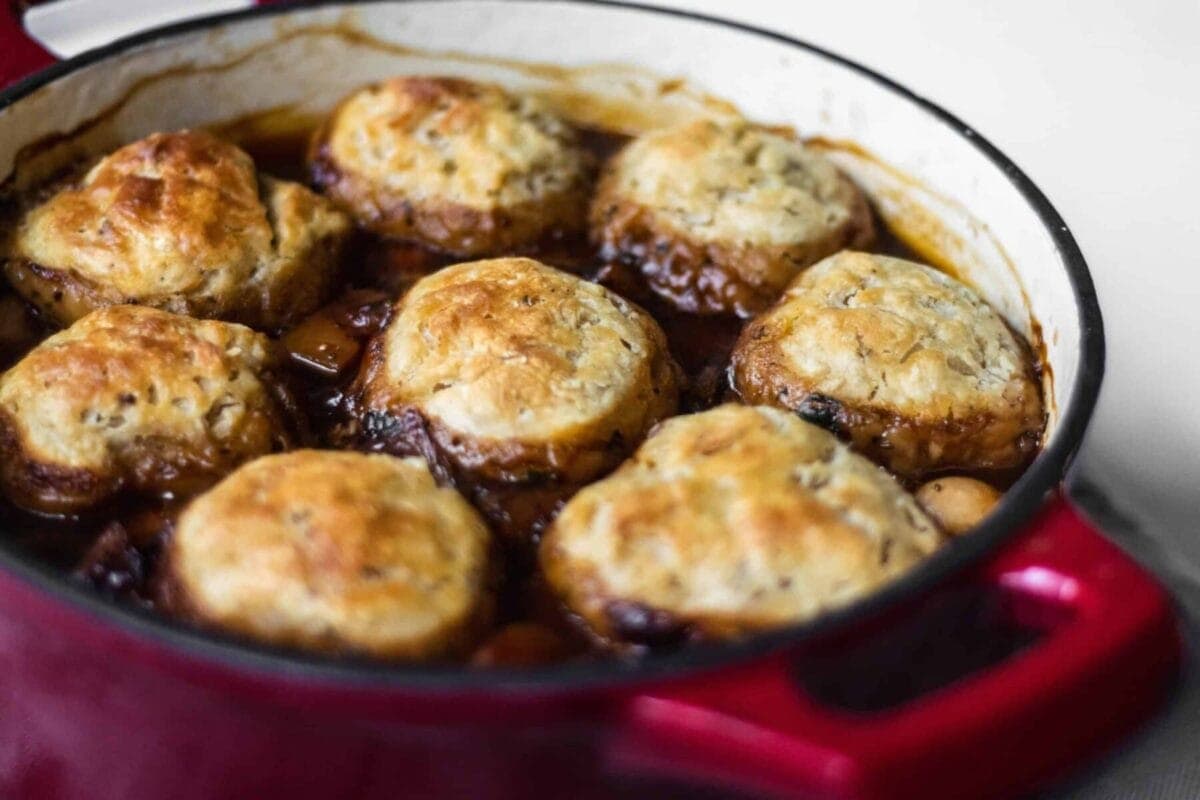 A red casserole dish full of vegan stew with crispy golden dumplings floating on top.