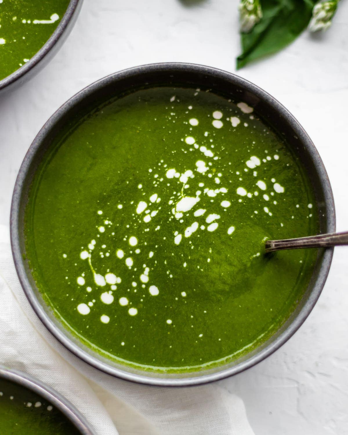 Overhead shot of a bowl of wild garlic soup, with cashew cream splattered the surface of the soup.