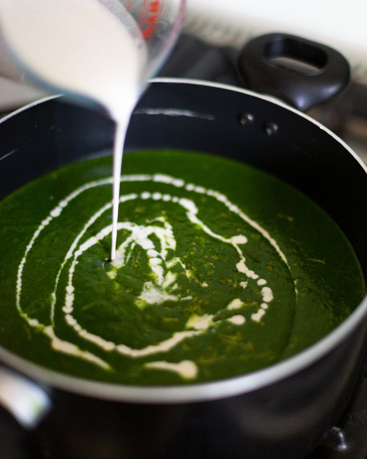 Saucepan full of blended soup with cashew cream being poured into it in a swirl.