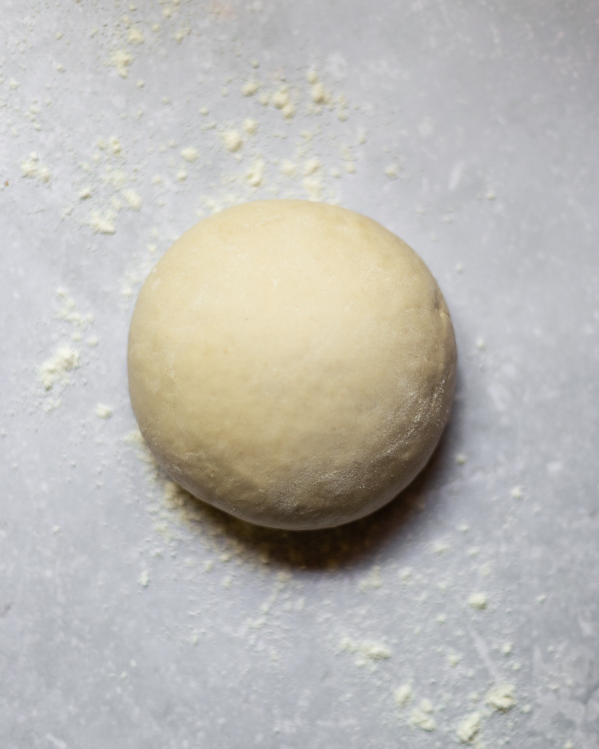 Ovehead image of a smooth ball of homemade vegan pasta dough on a grey background with extra flour dusted on top.