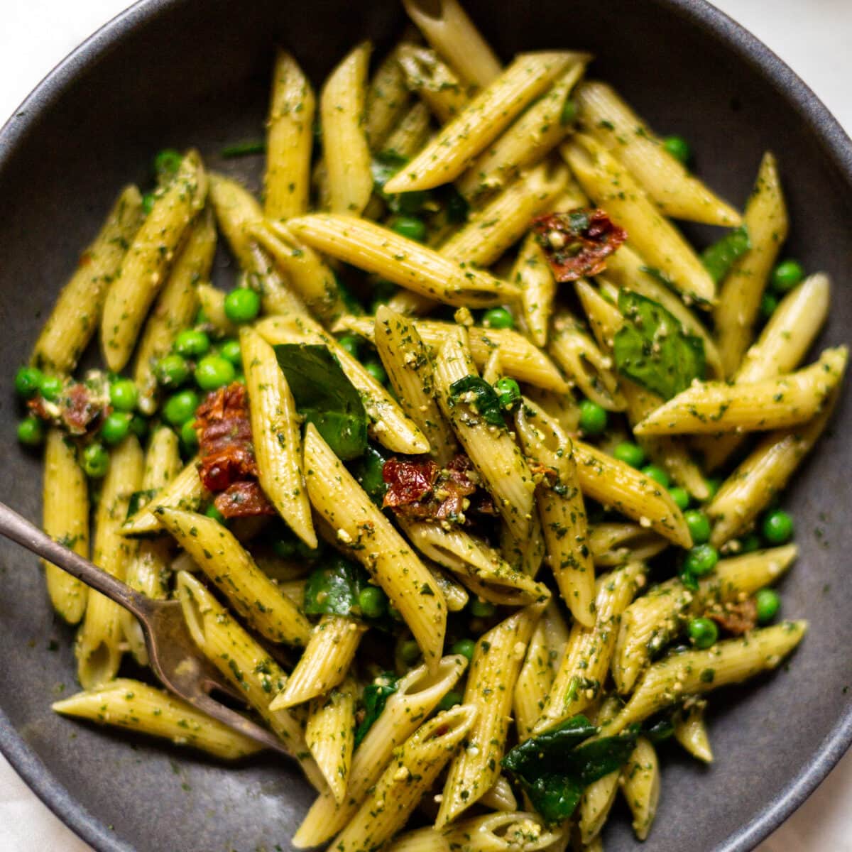 A photo looking down from above of a grey bowl filled with penne pesto pasta.