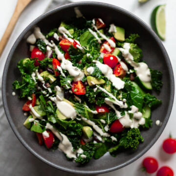 An overhead image of the Mexican kale salad drizzled with garlic cashew cream in a dark grey bowl.