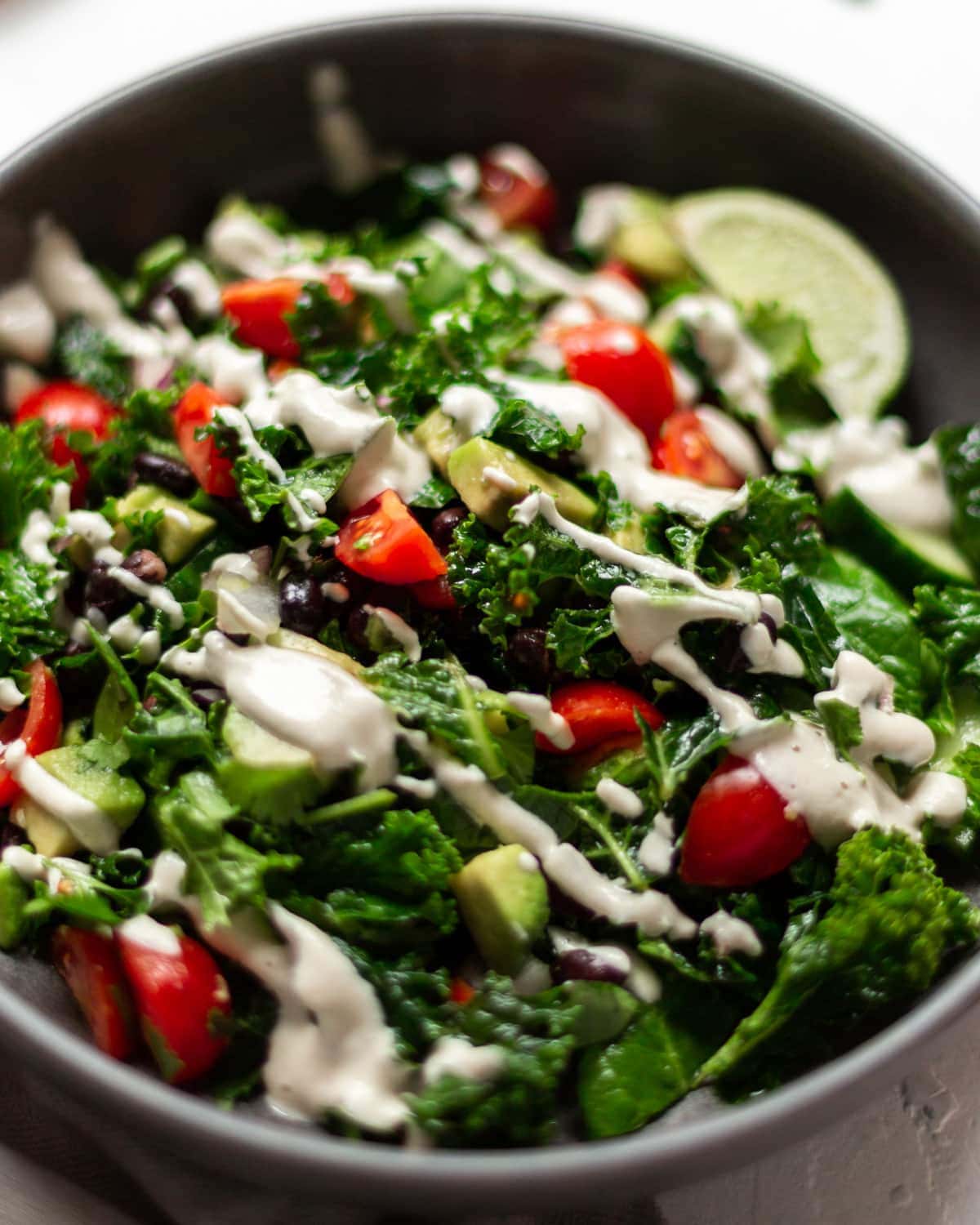 The Mexican kale salad with avocado, drizzled with garlic cashew cream, in a dark grey bowl on a white background.