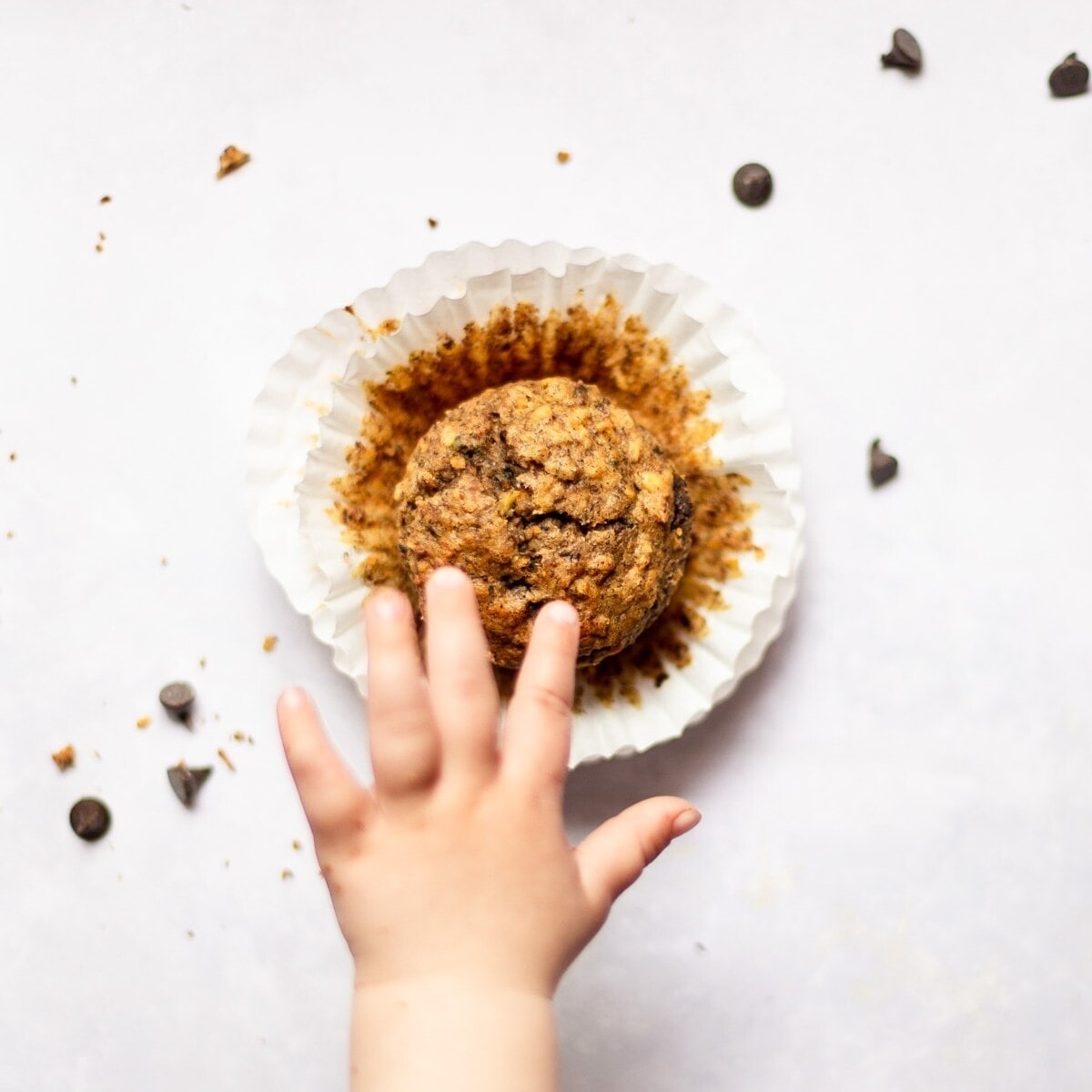 A babies hand reaching out to grab a single muffin.