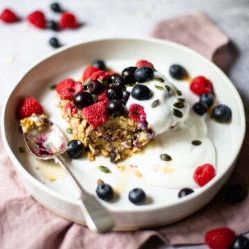 A bowl of baked oats, topped with extra fresh berries, coconut yoghurt, pumpkin seeds and maple syrup.