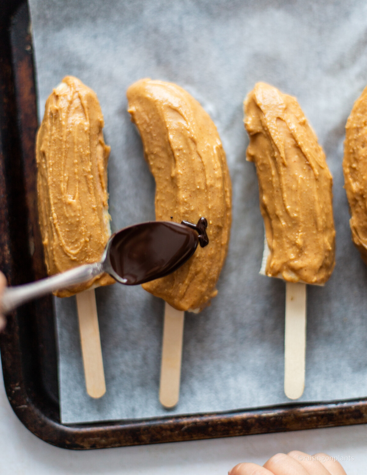 Drizzling chocolate over the peanut butter coated banana lollies, with a spoon. 